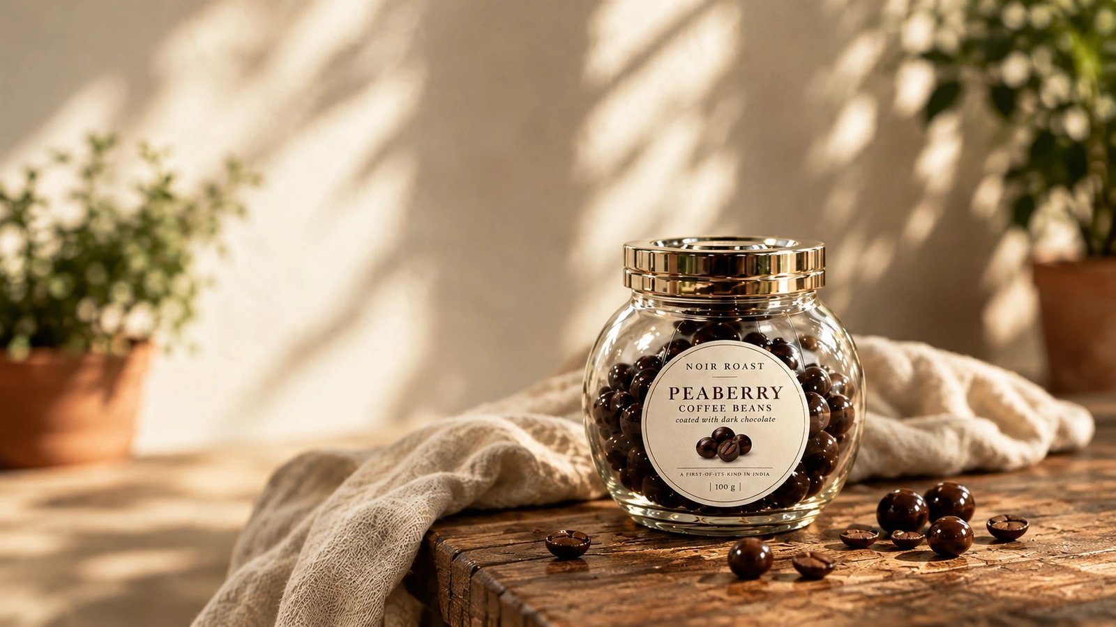 A glass jar of NOIR ROAST peaberry coffee beans coated in dark chocolate, on a rustic wooden table in warm sunlight